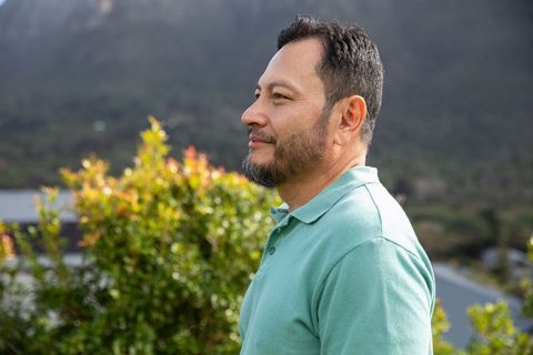 Thoughtful asian man standing in garden wearing mint polo looking into distance