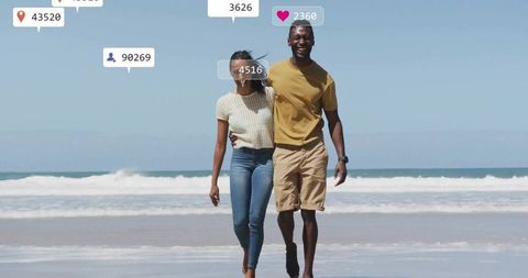 Smiling couple walking on sandy beach with social media icons, influencer lifestyle