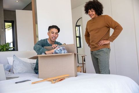 Roommates Unpacking Box with Linens in Bright Bedroom