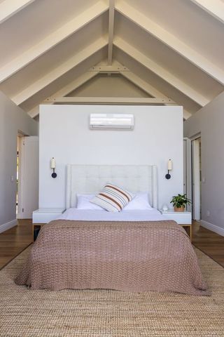 Sunlit minimalist master bedroom featuring vaulted beams, neutral bedding, jute rug