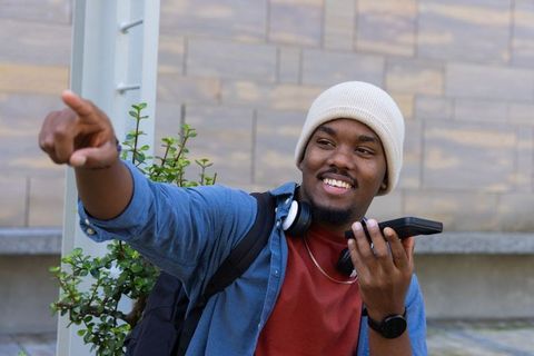 Young african american man pointing and using smartphone outdoors smiling with headphones