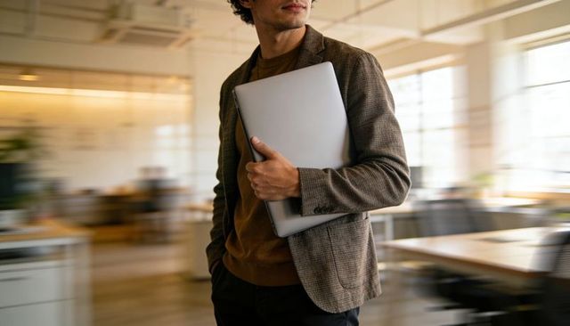 Walking professional holding laptop in modern open-plan co-working office with motion blur