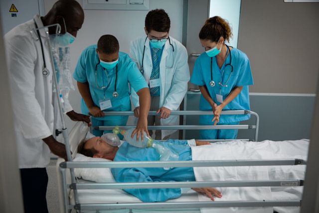 Diverse group of male and female doctors wearing face masks pushing patient in bed through corridor. medical and healthcare services at hospital during covid 19 pandemic.