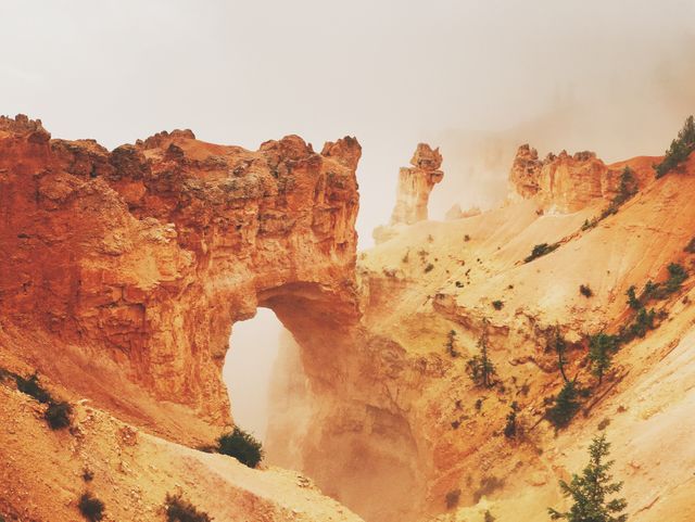 In this breathtaking stock photo, dramatic erosion has sculpted a natural arch in the rust-colored rocks of Bryce Canyon, Utah. This image features stunning geological formations framed by a soft mist, making it perfect for promoting travel, adventure tours, hiking excursions, or geological research. Ideal for nature enthusiasts and those looking to capture the raw beauty of the American Southwest.