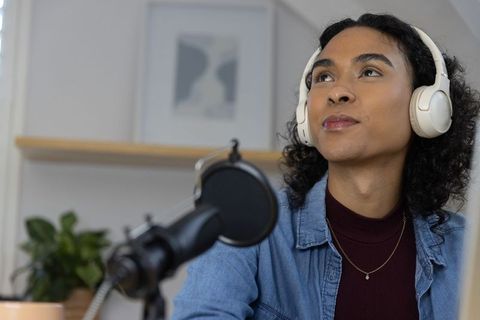 Nonbinary podcaster wearing headphones recording from cozy home studio with microphone