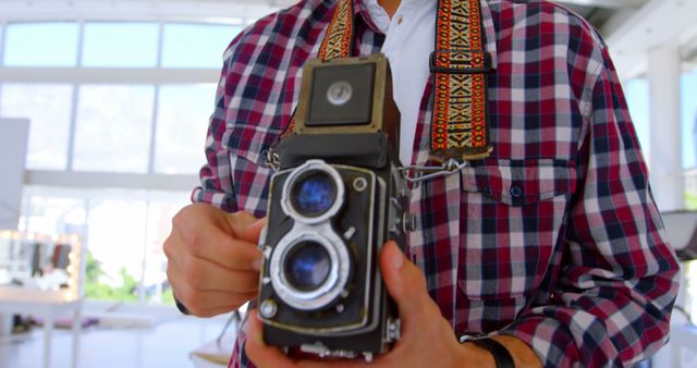 Caucasian man holds a vintage camera, with copy space. He stands indoors, showcasing a passion for classic photography equipment.