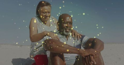 Mature couple embracing on sunlit beach with golden bokeh, relaxed coastal romance