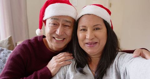 Diverse Couple Smiling in Santa Hats Celebrating Christmas at Home