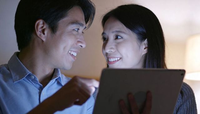 Smiling couple sharing tablet glow while leaning together in cozy living room evening