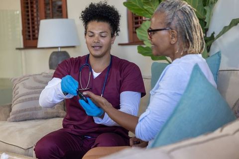 Home nurse checking senior african american woman fingertip with glucometer during visit