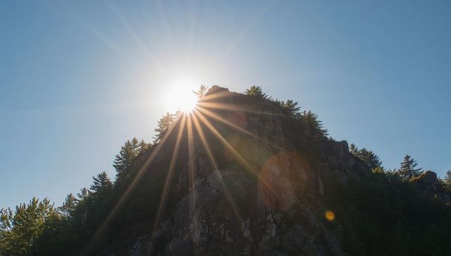 Sunburst crowning rocky mountain outcrop with pine trees and dramatic lens flare