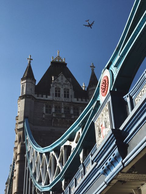 Tower Bridge in London seen from below with an airplane in the sky on a clear day. This image can be used for travel guides, tourism promotions, architecture studies, and showcasing London's iconic landmarks. Perfect for illustrating urban scenes, transportation, and city landscapes.