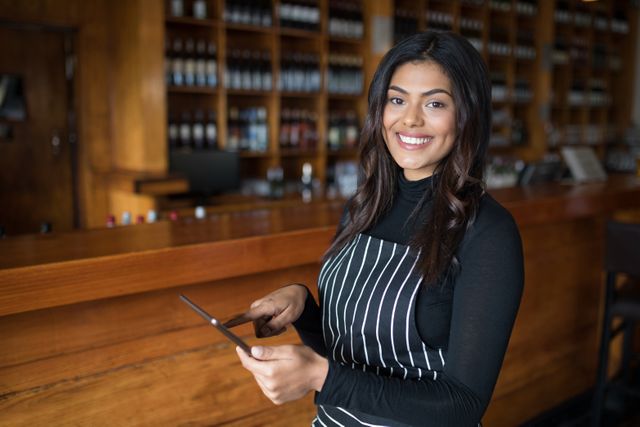 Portrait of smiling waitress using digital tablet at counter in bar