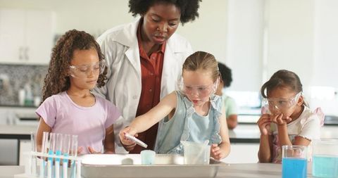 African american teacher guiding elementary girls doing safe science experiments in lab