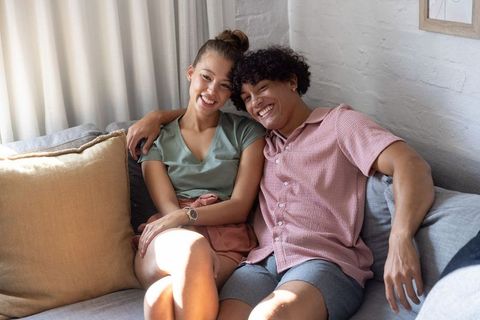 Young couple relaxing on cozy sofa, smiling and basking in warm natural sunlight