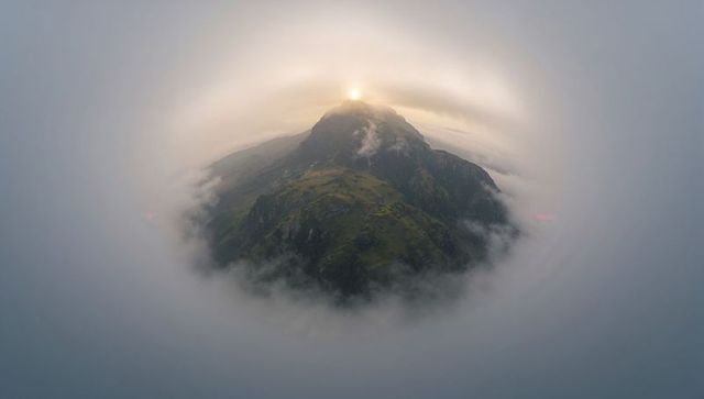 Sun halo crowning solitary mountain peak rising through circular cloud ring at dawn