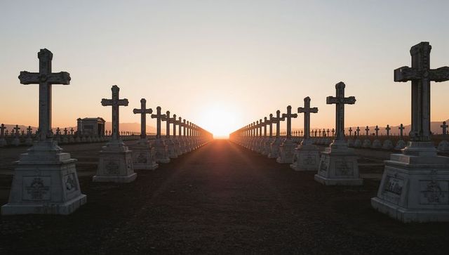 Sunrise aligning symmetrical rows of stone crosses leading down cemetery avenue