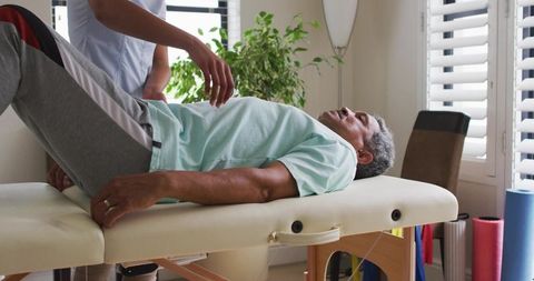Senior patient receiving hip mobilization therapy on padded treatment table with clinician
