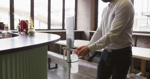 Person using hand sanitizer dispenser in modern cafe setting. Highlights hygiene and safety protocol in public space. Useful for promoting cleanliness, public health awareness, coronavirus prevention, and maintaining hygiene in businesses and cafes.