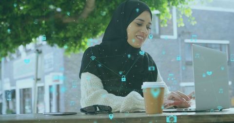 Hijabi Woman Using Laptop at Outdoor Cafe with Digital Interface