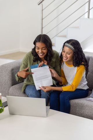 Diverse mother and teen daughter reviewing letter and celebrating good news at home