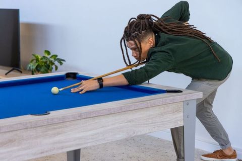 African american man aiming cue on blue pool table in modern minimalist living room