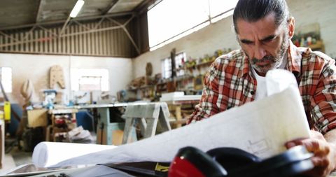 Carpenter reviewing blueprint in wood workshop