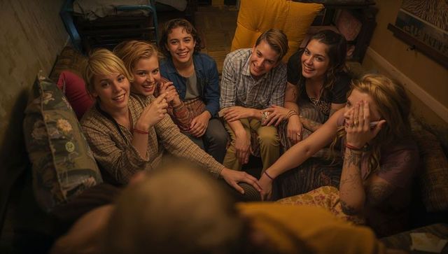 Cozy late-night friends leaning in, laughing and connecting on patterned sofa with warm light