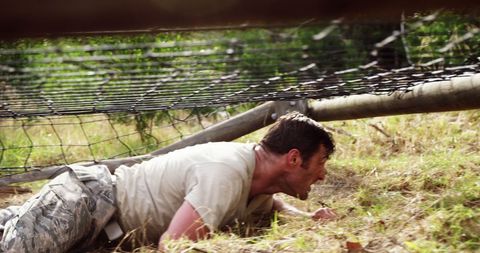 Man crawling under wire in intense military training exercise