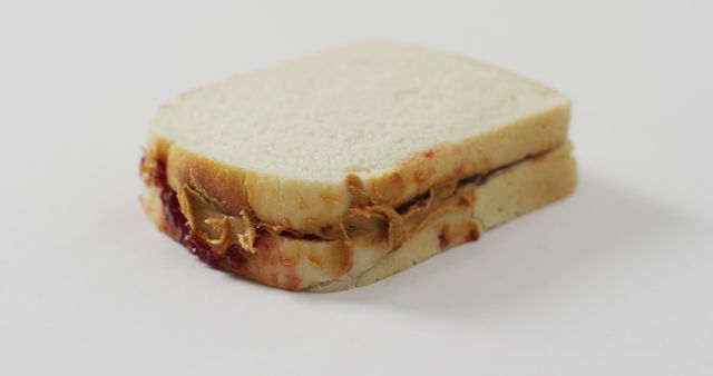 Close-up image of a classic peanut butter and jelly sandwich against a white background. Ideal for articles on simple lunch ideas, nutrition, or kid-friendly recipes. Can be used in promotional materials for food products or culinary blogs.