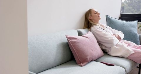 Young woman relaxing on modern pastel sofa with tv remote and cushions