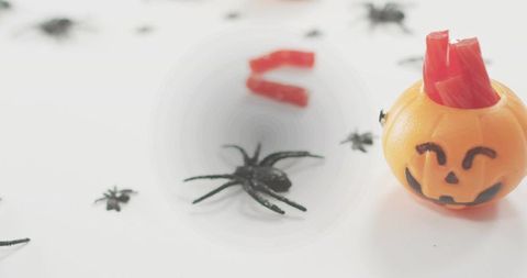 Whimsical halloween pumpkin holding red gummy strips with scattered black spiders on white
