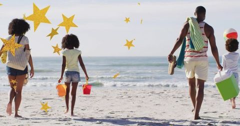 Family walking toward ocean carrying beach gear under golden stars
