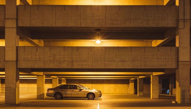 Silver sedan sitting under warm light in multi-level concrete parking garage at night