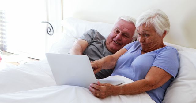 Senior couple lying in bed using laptop together engaged and smiling - Download Free Stock Images Pikwizard.com