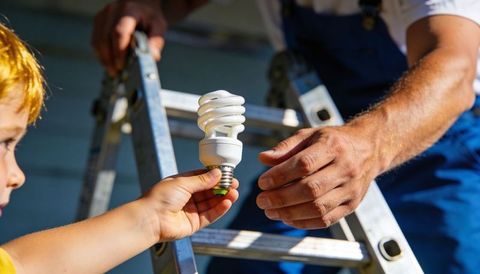 Child passing spiral cfl bulb to adult on ladder teaching home electricity safety outdoors