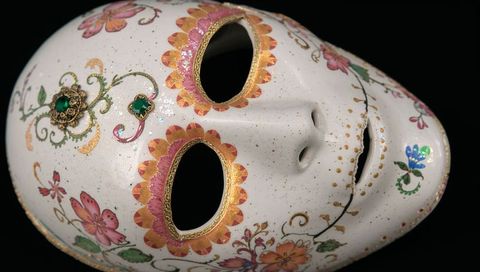 Decorative porcelain mask featuring gilded trim, floral painting and green jewel accents