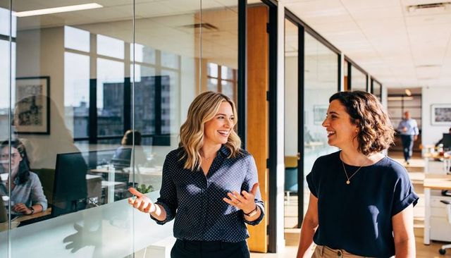 Coworkers walking and talking in modern office with glass partitions and daylight