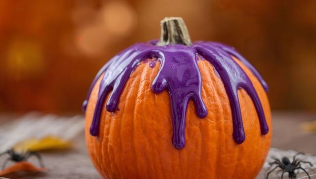 Decorated pumpkin dripping purple paint on rustic tabletop