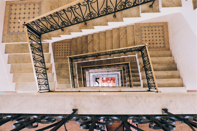 View showcasing a downward spiral perspective of marble staircase with ornate metal railings and geometric design. This could be used for topics related to interior design, architecture, modern buildings, or geometric aesthetics. Suitable for articles, blogs, and websites focusing on innovative building designs or architectural photography.