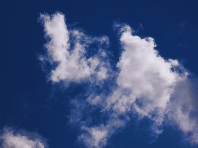 This image captures fluffy white clouds floating under a clear blue sky. It can be used to illustrate weather conditions, evoke feelings of calmness and serenity, or serve as a background for various nature-related themes.