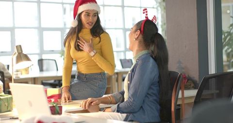 Festive office coworkers chatting and celebrating holiday season with Santa hat and gifts