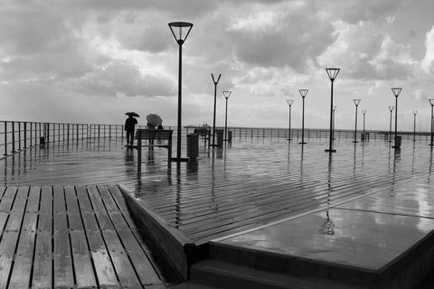 Couple with Umbrellas on Rainy Waterfront Boardwalk