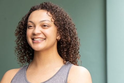 African american woman smiling with curly hair wearing grey tank and gold hoop earring