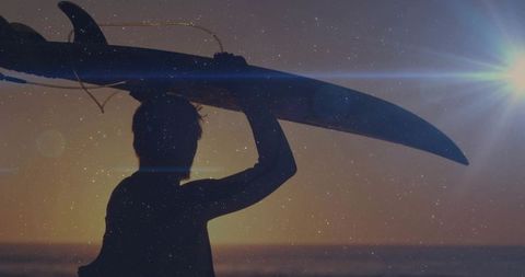 Male surfer carrying longboard overhead at sunset silhouette with lens flare golden hour