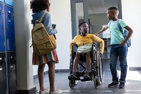 Elementary students supporting wheelchair classmate in school corridor near lockers