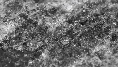Macro sparkling crystal granules on dark pavement revealing gritty texture monochrome