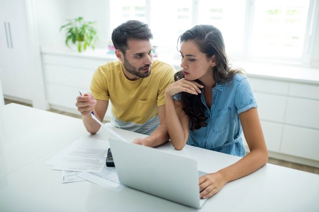 Worried couple calculating their bills with laptop in the kitchen at home
