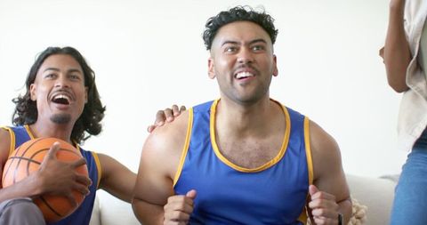 African american friends cheering during basketball watch party on couch in living room