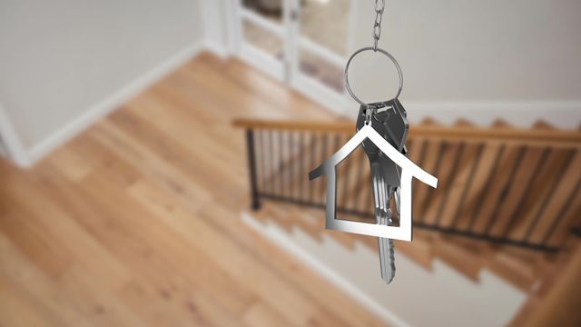 House key dangling over a wooden staircase in a modern home. Perfect for real estate promotions, home ownership campaigns, housewarming announcements, and interior design concepts.